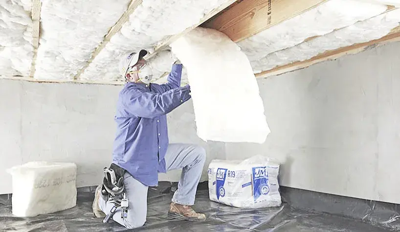 Technician fitting insulation batts in a crawl space